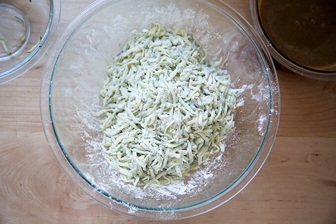 Grated zucchini tossed in flour in a large bowl.