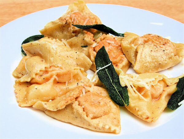 A plate of just-cooked pumpkin ravioli with sage brown butter on a plate. 