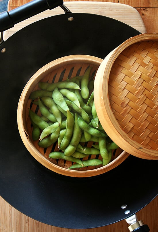 Edamame steaming in a bamboo steamer basket in a wok.