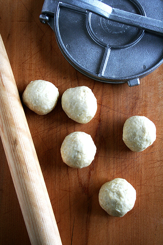 tortilla dough balls aside a rolling pin and a tortilla press