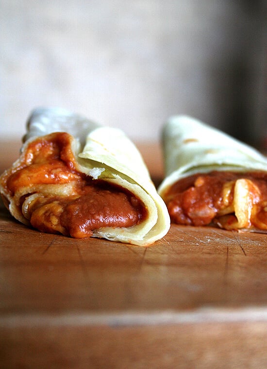 Two bean and cheese burritos, made with homemade flour tortillas, on a board.