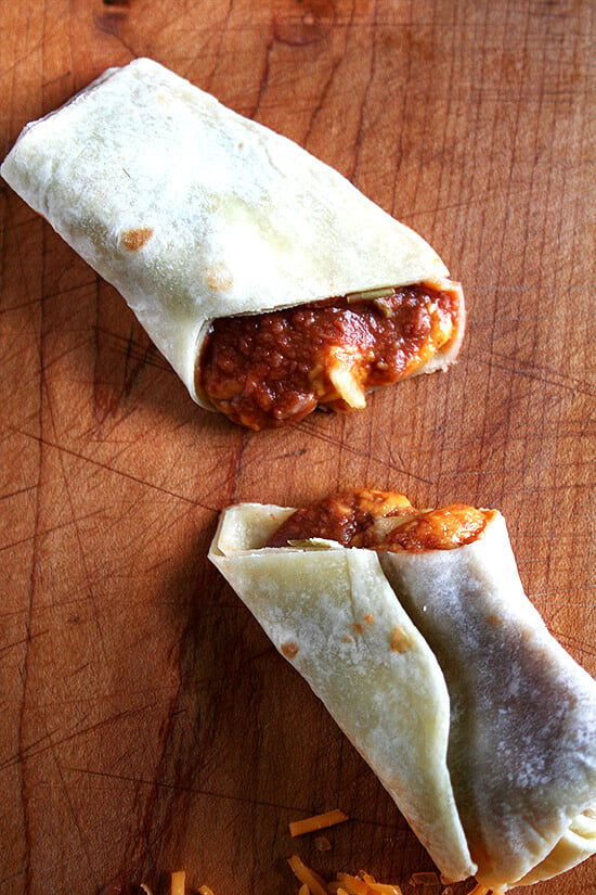 A halved bean and cheese burrito made with homemade flour tortillas on a board.