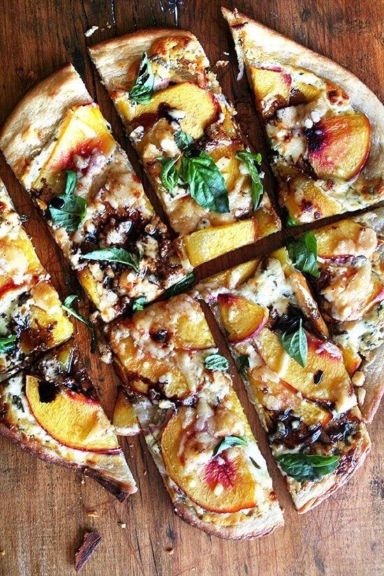 Just-baked nectarine pizza on a board, sliced into pieces. 