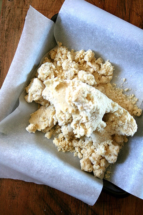 A parchment-lined square baking dish filled with the rosemary shortbread dough.