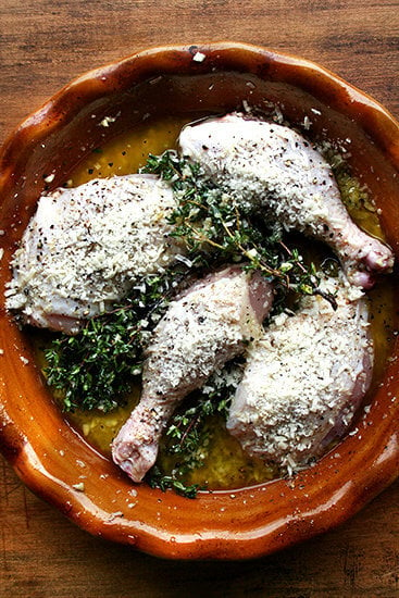 An overhead shot of uncooked chicken legs in a pie plate with parmesan, thyme, olive oil, and white wine. 