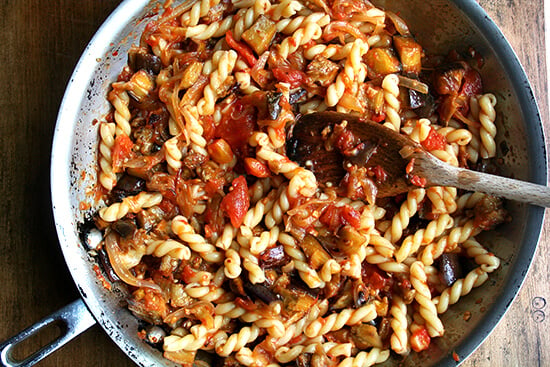 A sauté pan filled with roasted eggplant and tomato pasta. 