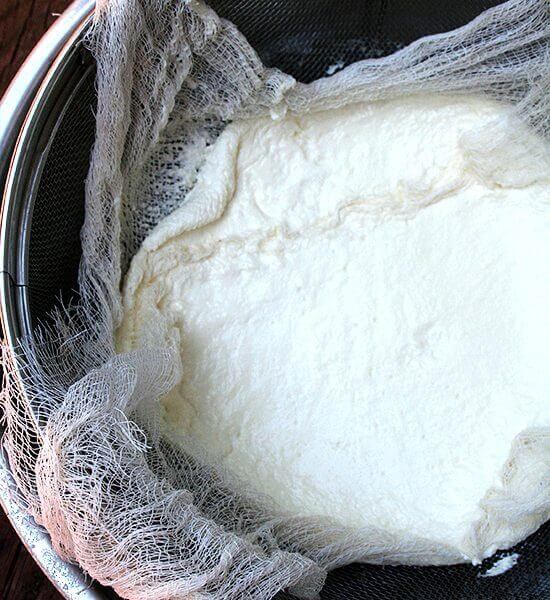 A cheese cloth-lined sieve holding homemade ricotta.