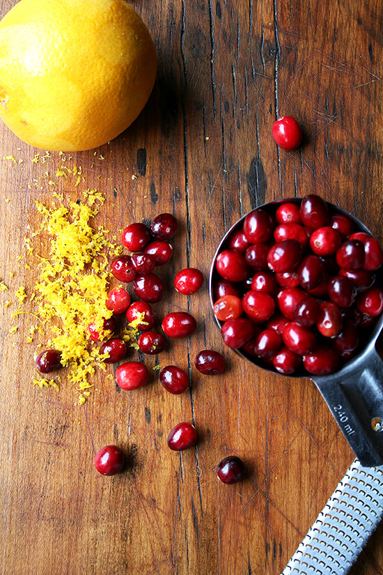 Cranberries and orange zest on a cutting board.