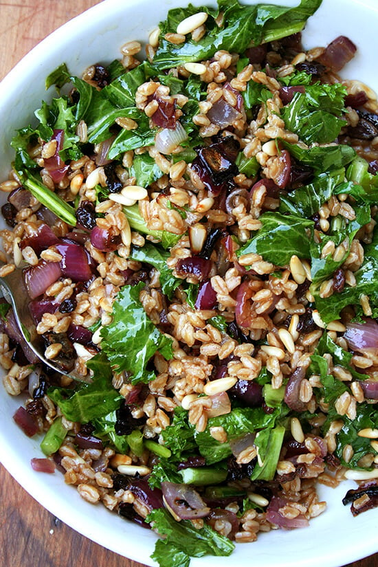 A bowl of farro salad with roasted onions, toasted pine nuts, and wilted mustard greens.