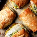 Five baked spanakopita strudels on a sheet pan.
