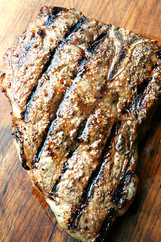 A grilled grass-fed t-bone steak, resting on a cutting board. 