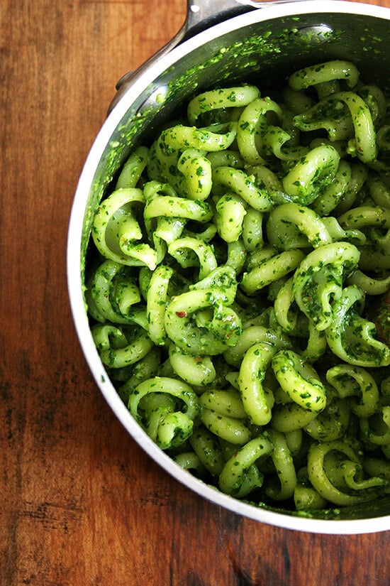 A pot filled with pasta and pesto sauce. 