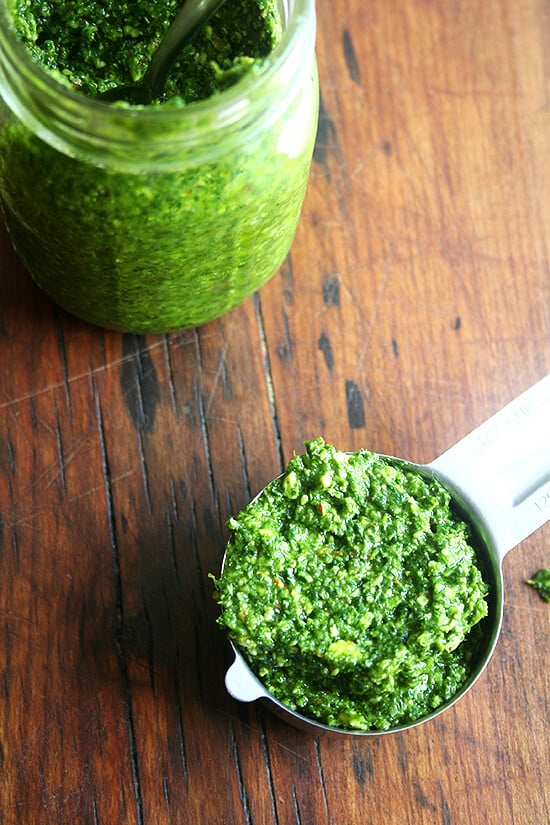A measuring cup filled with pesto sauce aside a jar of homemade pesto sauce. 