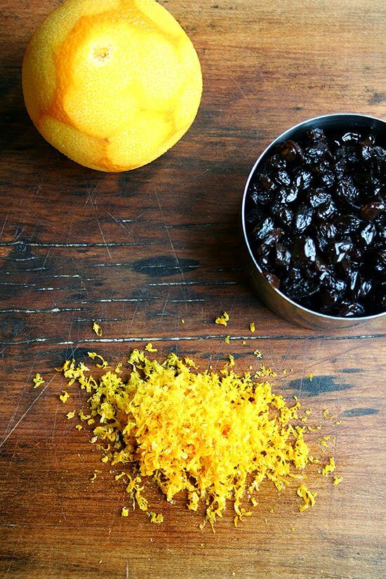 A board with a zested orange and simmered raisins.