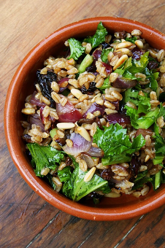 A bowl of farro salad with roasted onions, toasted pine nuts, and wilted mustard greens.