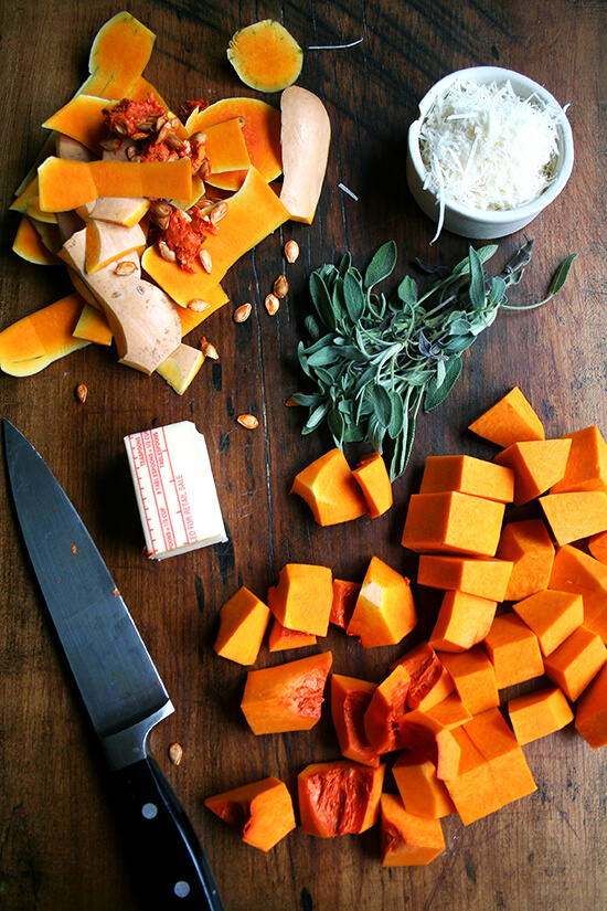 A board with ingredients for butternut squash pasta sauce: peeled butternut squash and sage. 