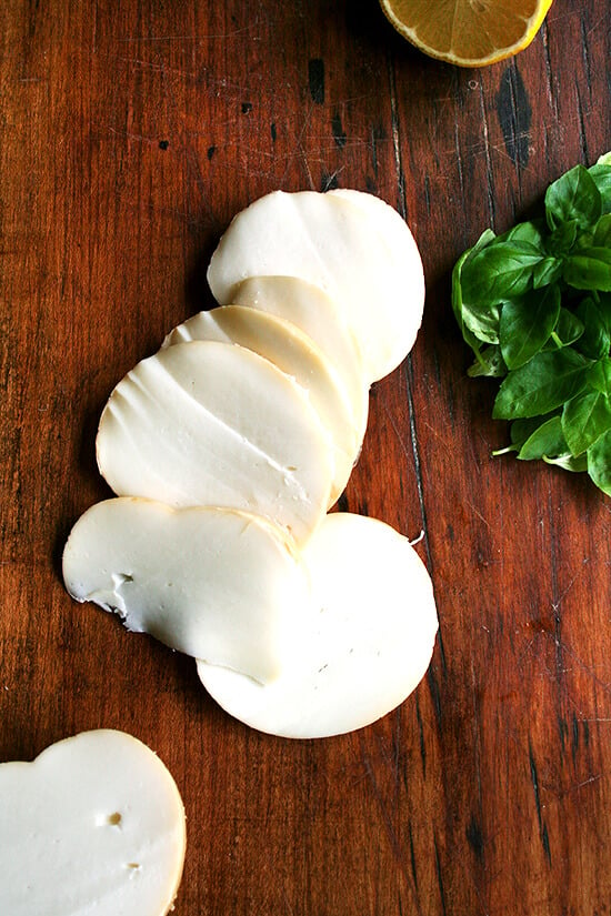 Sliced smoked mozzarella on a board.