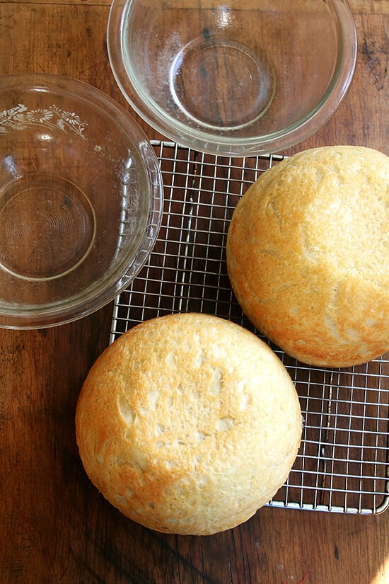 Two fresh loaves of peasant bread, two glass pyrex bowls, and cooling rack