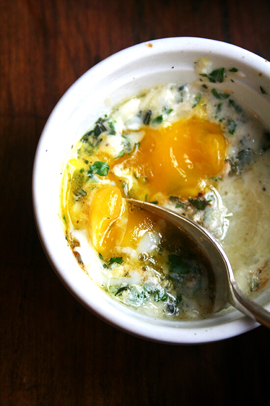 A ramekin holding a baked (shirred egg) with a spoon.