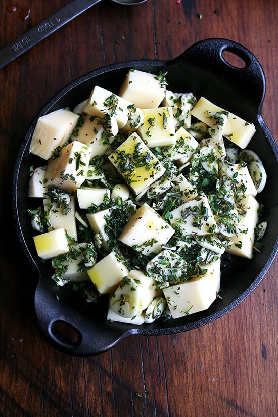 cubed fontina, herbs, olive oil, garlic & salt in a cast iron skillet on a board.