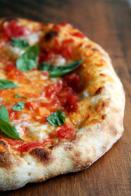 Just-baked Margherita pizza on a board topped with basil.