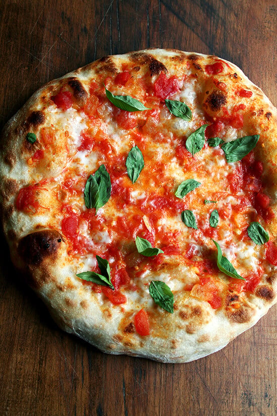 Just-baked Margherita pizza on a pizza peel topped with basil.