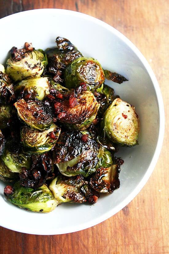 Close-up overhead view of brussel sprouts roasted with olive oil, salt and pepper, and crispy pancetta in a small white serving bowl.