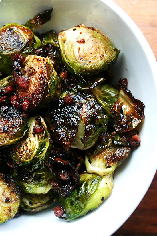 Overhead close-up of brussel sprouts roasted with olive oil, salt and pepper, and crispy pancetta in a white serving bowl.