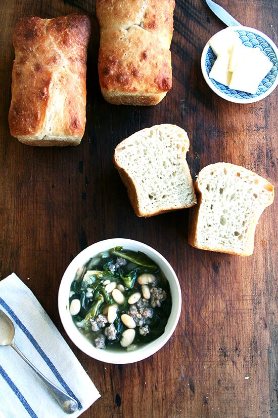 A bowl of white bean, sausage, and escarole soup aside  homemade peasant bread.