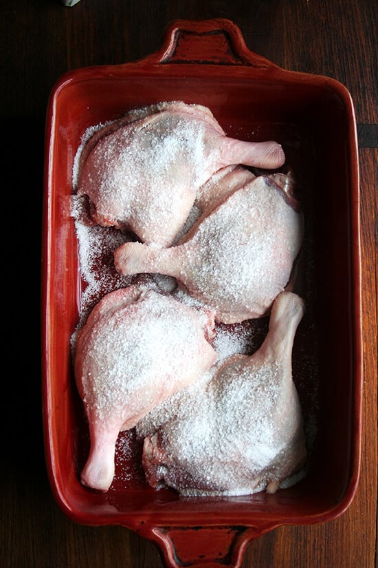 Four duck legs in a 9x13-inch red baking dish sprinkled with salt.