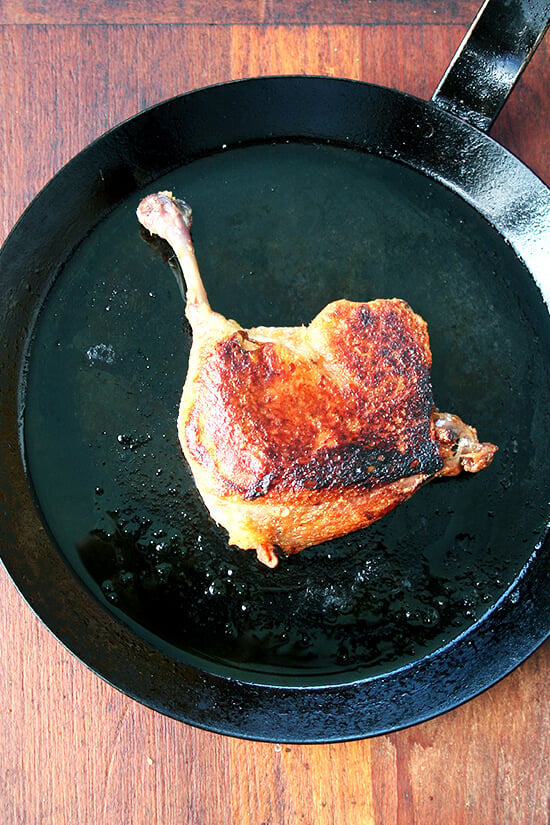 A seared duck leg confit in a cast iron skillet. 