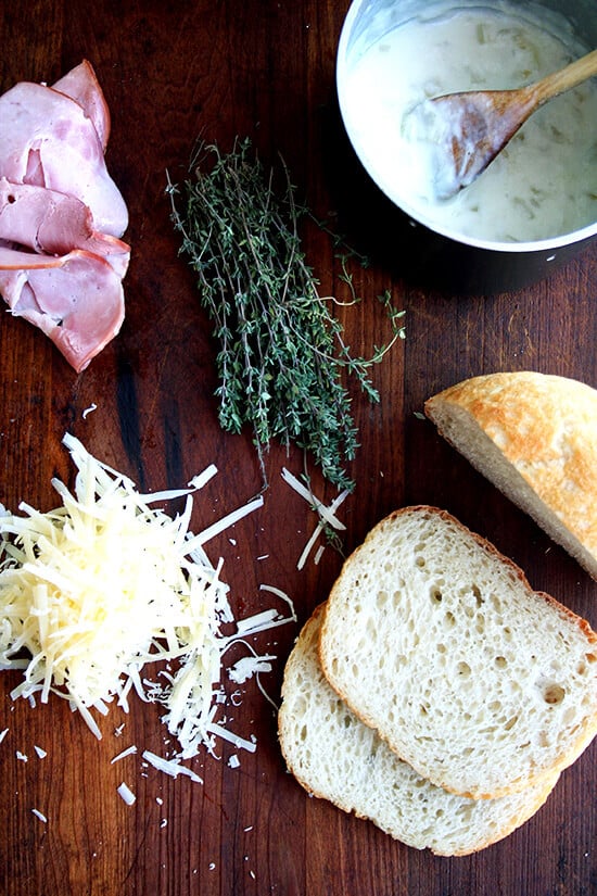 Croque monsieur ingredients on a board: ham, Gruyère, thyme, bread, béchamel.