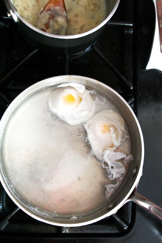 Two eggs poaching in a pot on the stovetop. 