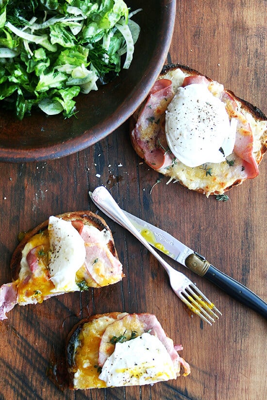 A bowl of salad aside a halved croque madame. 