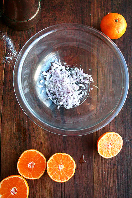 Clementine dressing in the making: A bowl of minced shallots seasoned with salt and two halved clementines. 