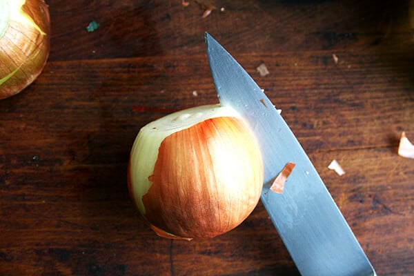 An onion on a board with a knife inserted into the outer layer.