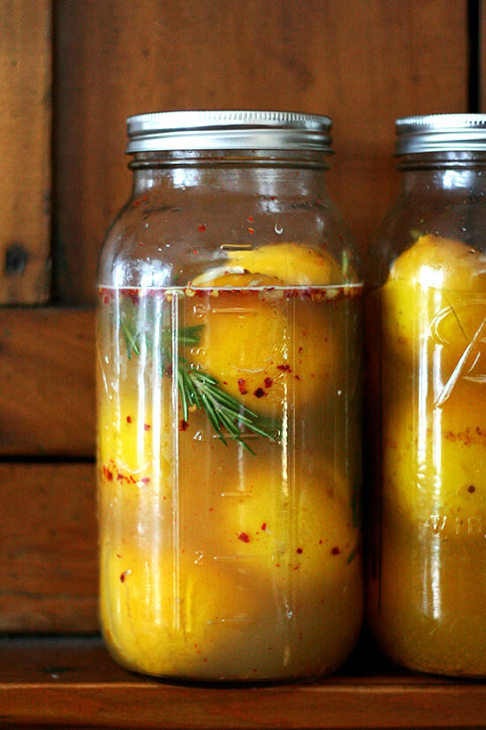 Two jars of preserved lemons standing on a shelf. 