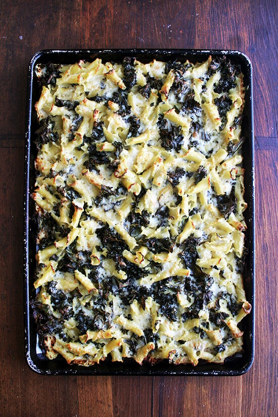 An overhead shot of just-baked pasta gratin with kale on a sheet pan.