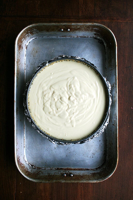 Cheesecake pan filled with batter set in larger pan, ready for water bath.