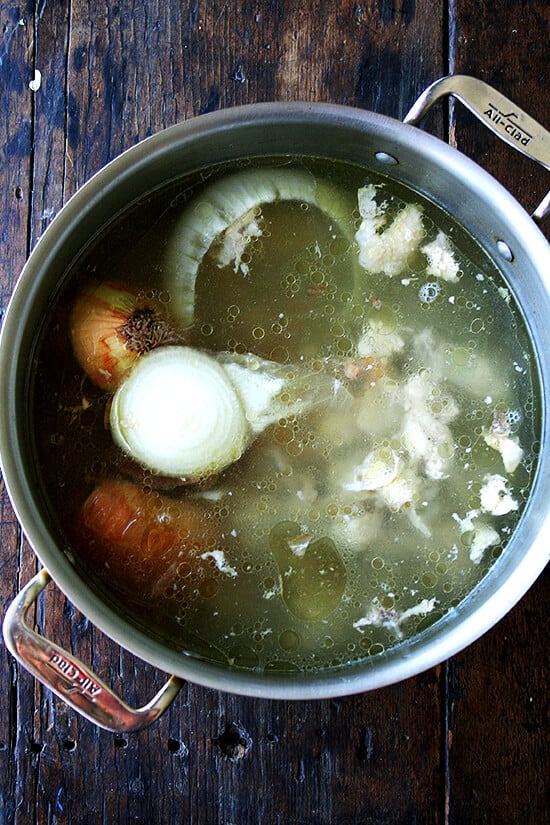 A stock pot filled with onions and chicken scraps. 