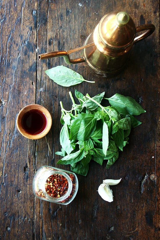sauce ingredients on a board: olive oil, vinegar, herbs, garlic, crushed red pepper flakes.