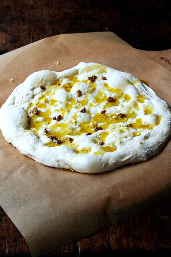 A pizza dough round topped with oil, garlic, anchovy.