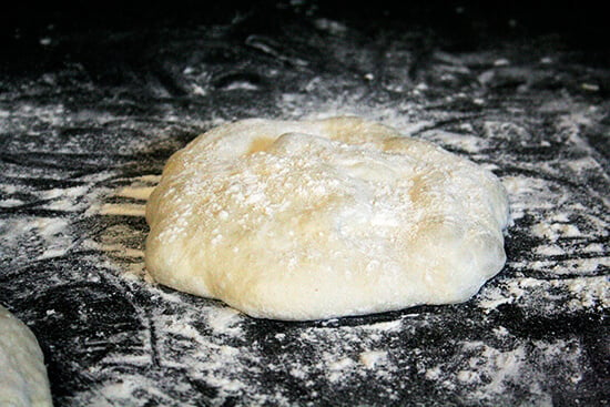 A round of pizza dough resting on a board. 