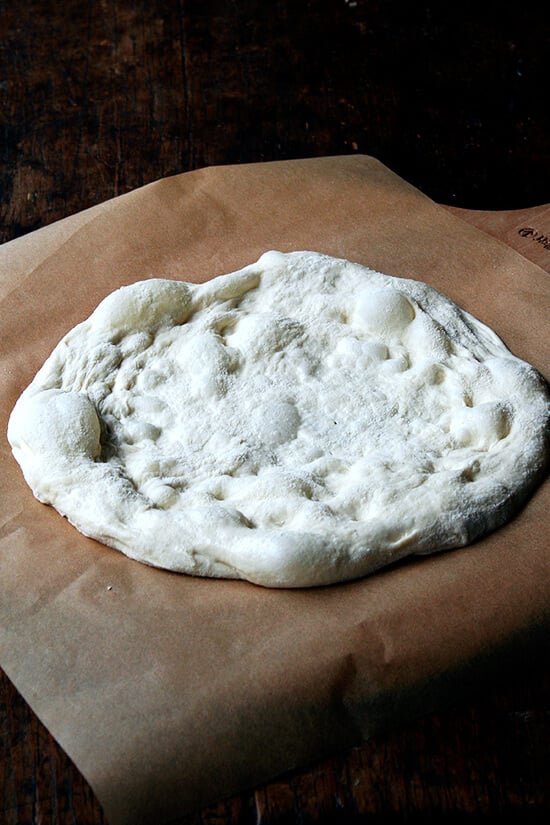 A stretched round of Jim Lahey pizza dough on a parchment-lined peel. 