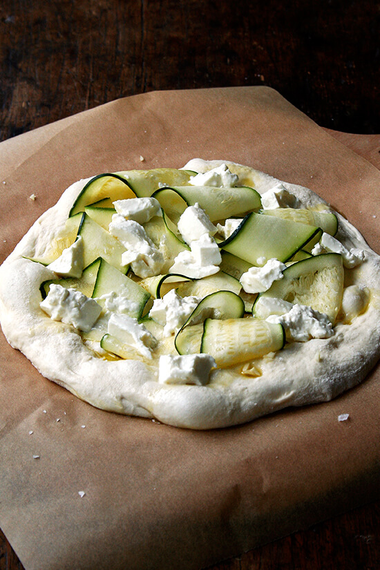 The zucchini anchovy pizza, ready for the oven, on a parchment-lined pizza peel. 