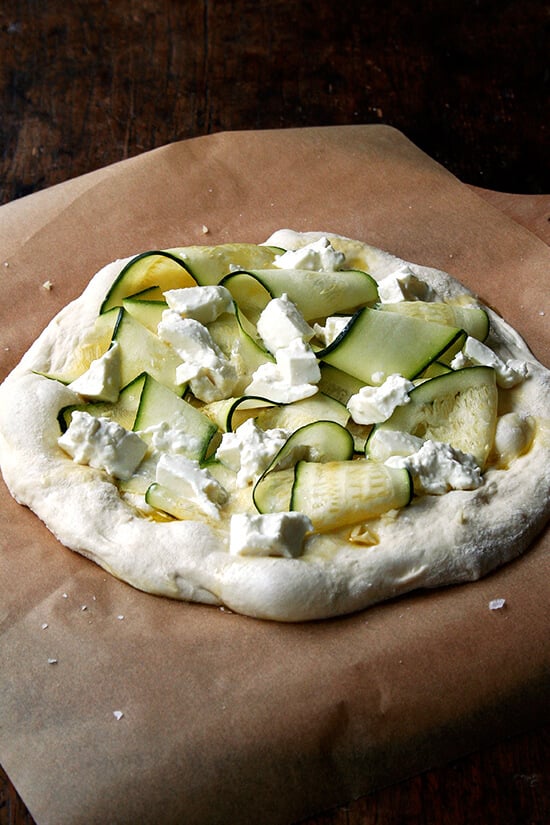 The zucchini anchovy pizza, ready for the oven, on a parchment-lined pizza peel. 