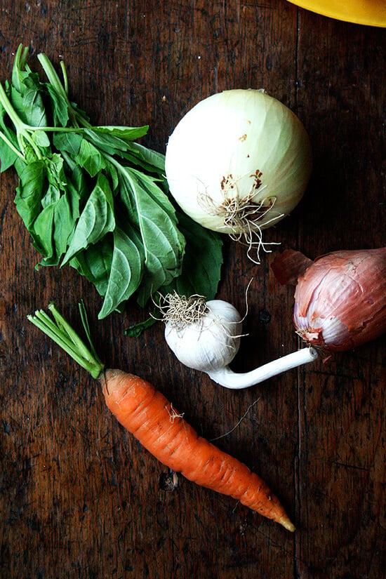 A table of basil, onion, garlic, shallot, and carrot.