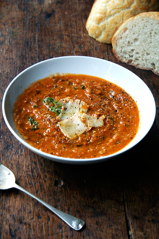 A bowl of roasted tomato and bread soup aside homemade bread and a spoon.