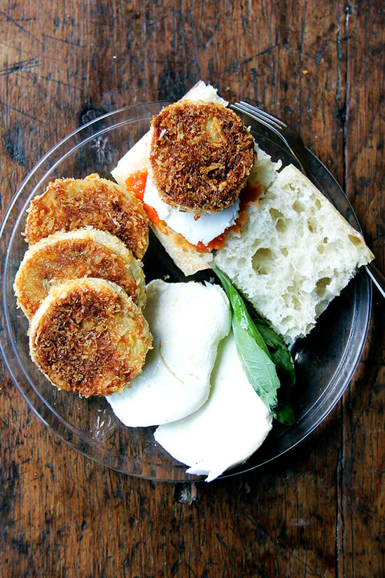 A plate of crispy eggplant rounds, tomato, mozzarella, bread, and basil. 