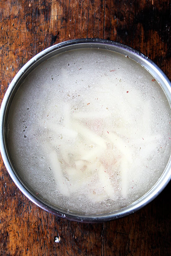 Eine Schüssel mit eingeweichten Kartoffeln in heißem Wasser. 